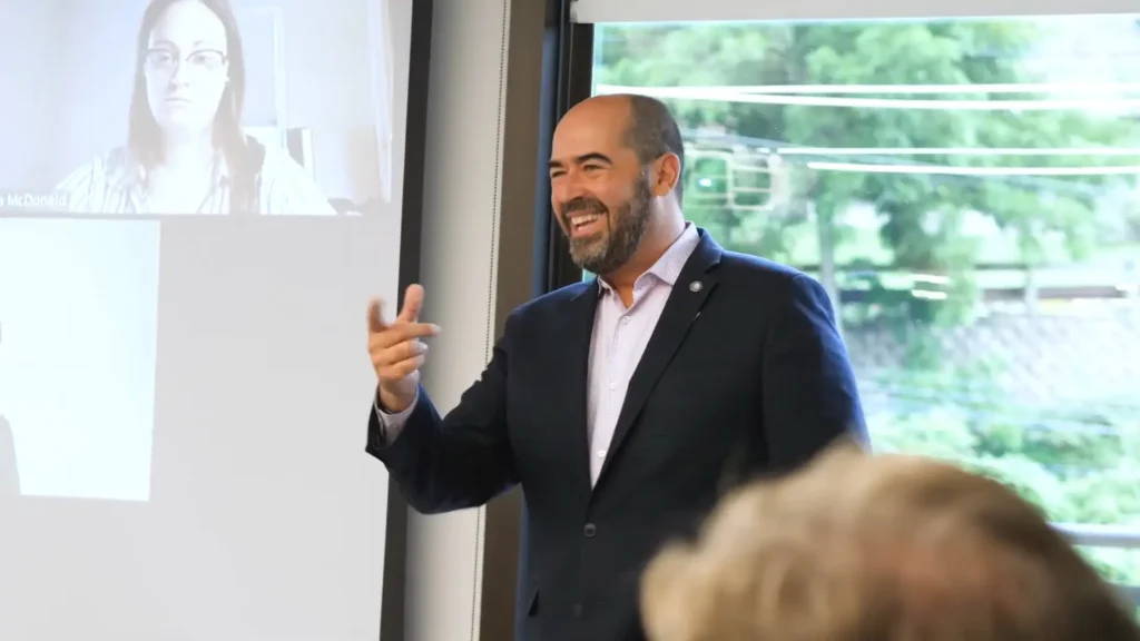 Alex Archawski speaking to a group, smiling and pointing